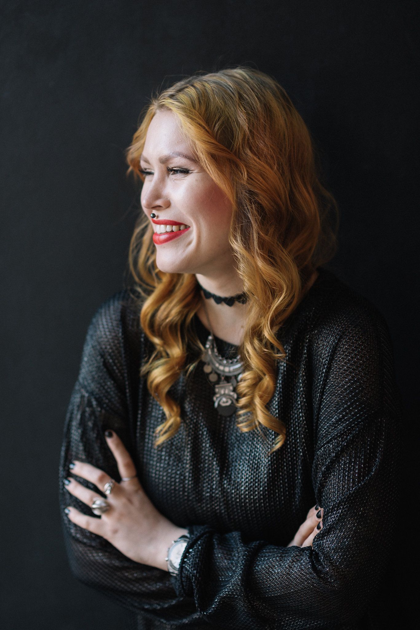 Studio portrait with flowing auburn curls and elegant statement jewelry against dark backdrop.
