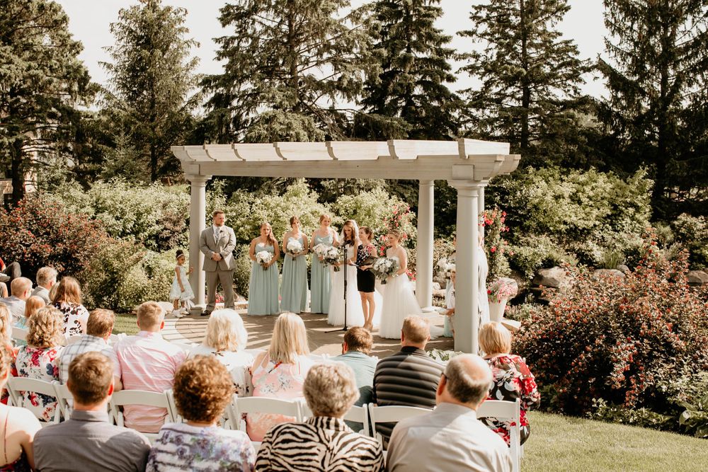 Guests seated at an outdoor wedding ceremony with a white pergola adorned with colorful flowers and greenery.
