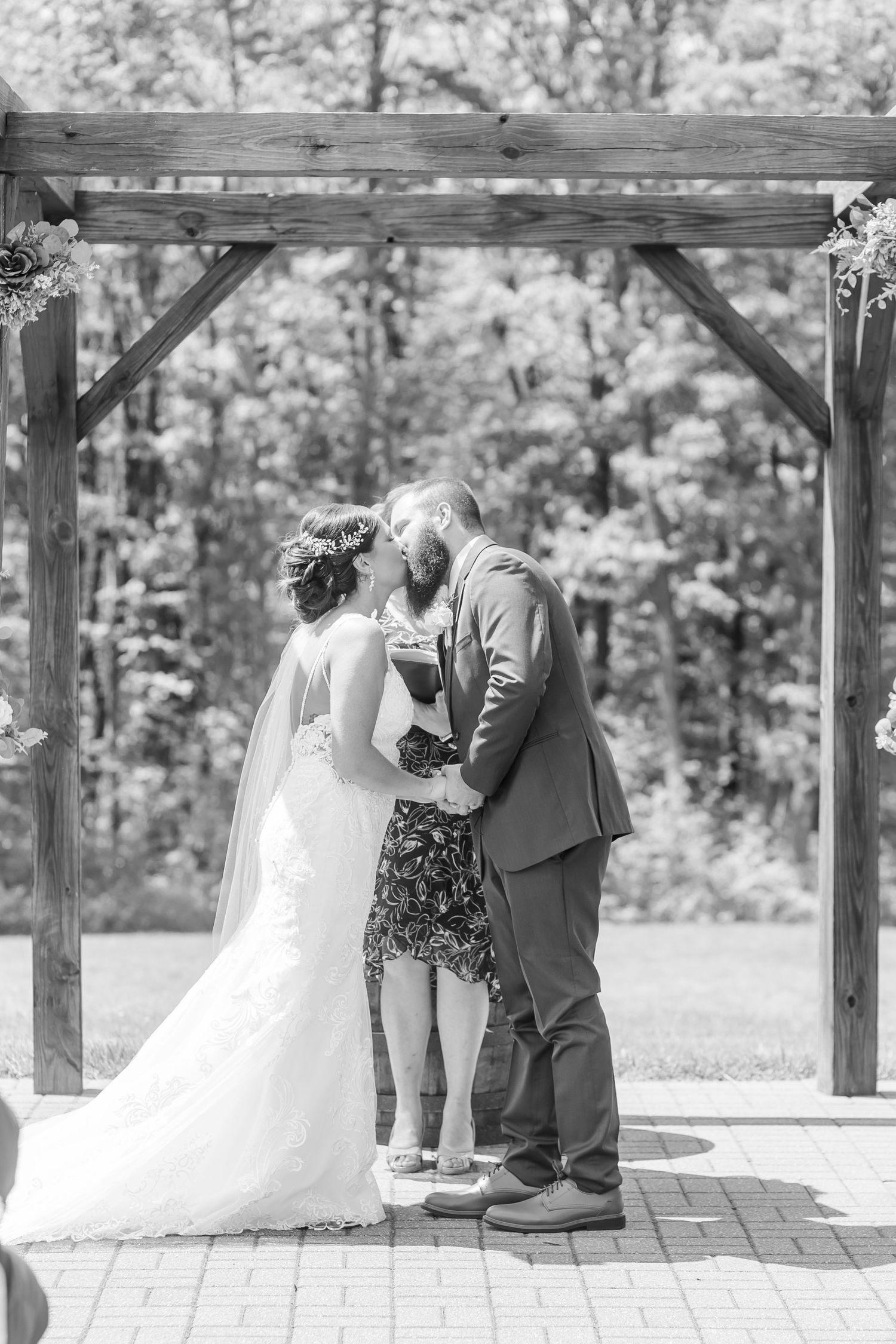 Black and white photo of a couple during their wedding ceremony under a wooden pergola.