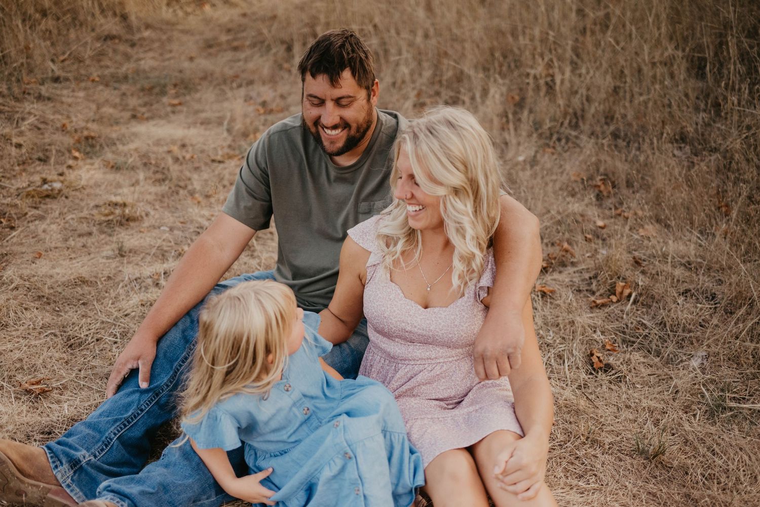 Family enjoying a tender moment together while sitting in a dry grassy field.