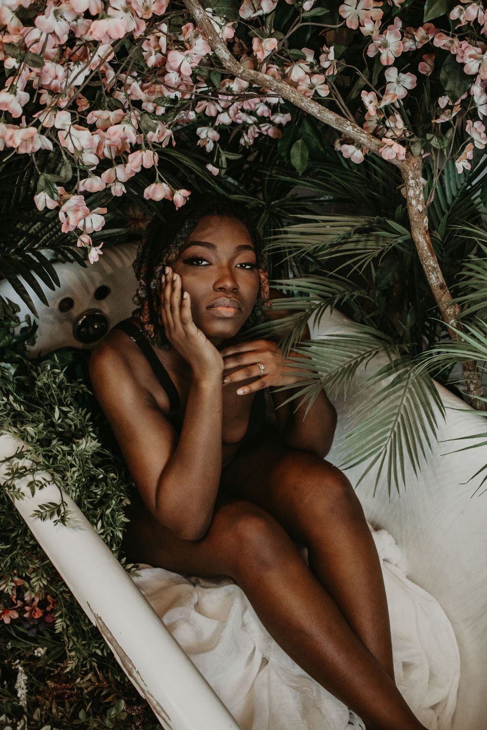 Ethereal portrait in a vintage bathtub with pink cherry blossoms and tropical leaves.