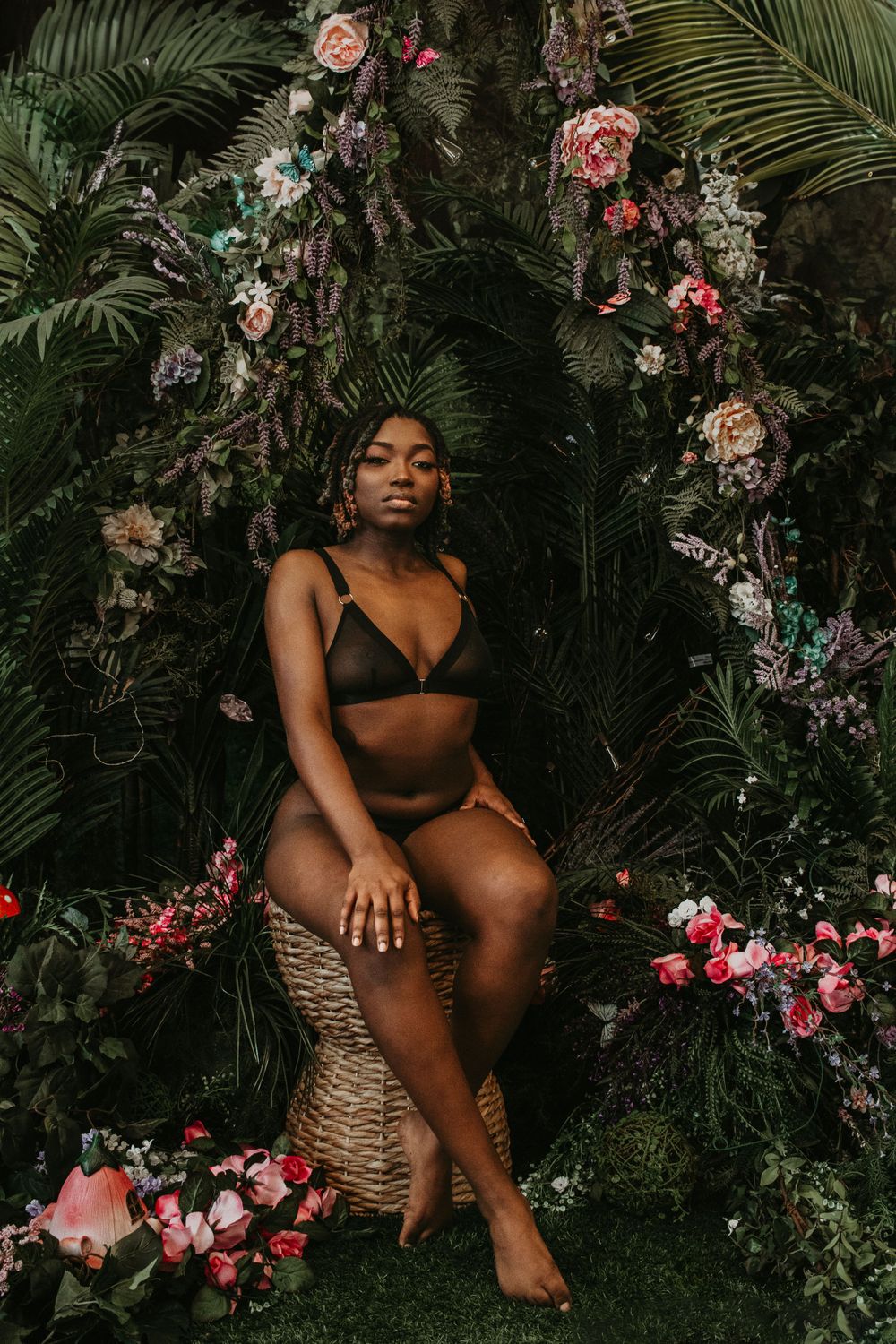 Tropical garden boudoir portrait with floral arch and palm leaves.