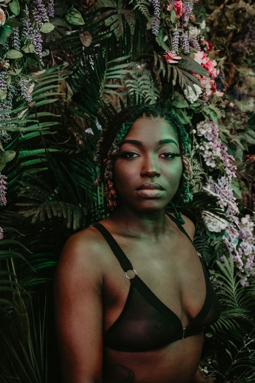 Ethereal portrait among ferns and flowers with dramatic green lighting.