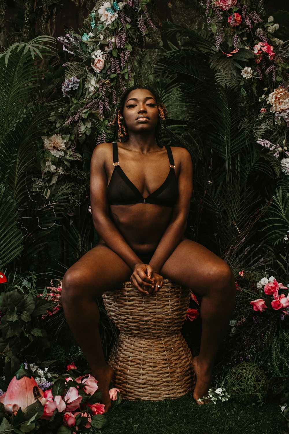 Artistic boudoir photoshoot in a lush garden setting with tropical foliage and pink flowers.