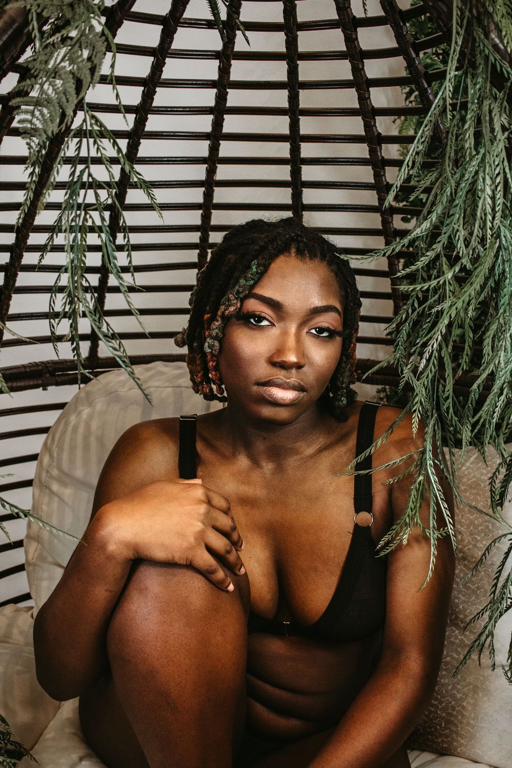 Moody portrait in a hanging chair surrounded by cascading greenery and natural light.