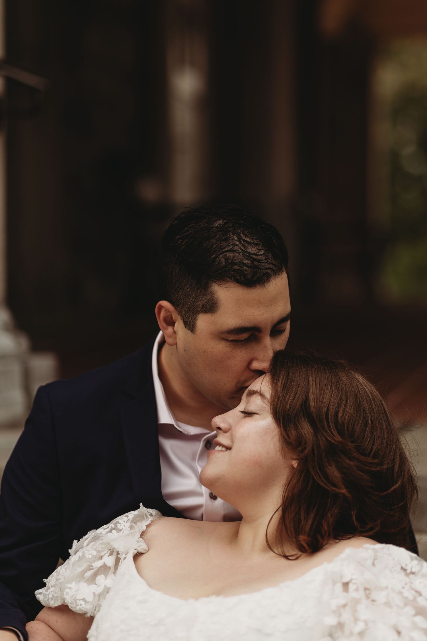 A romantic wedding moment captured in moody lighting as a couple shares an intimate embrace.