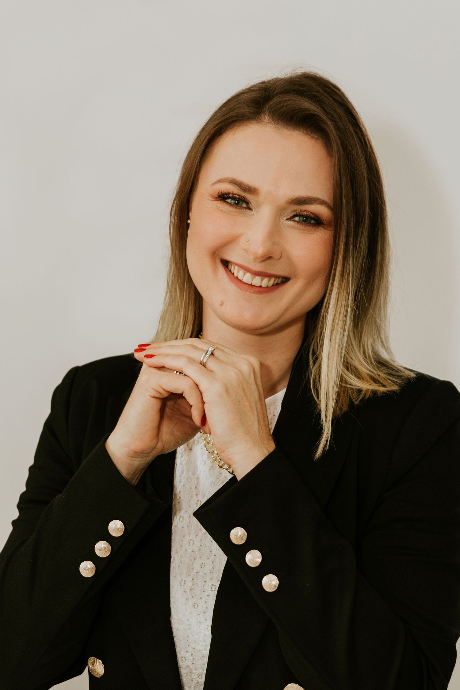 Professional headshot featuring black blazer with pearl buttons against neutral background.