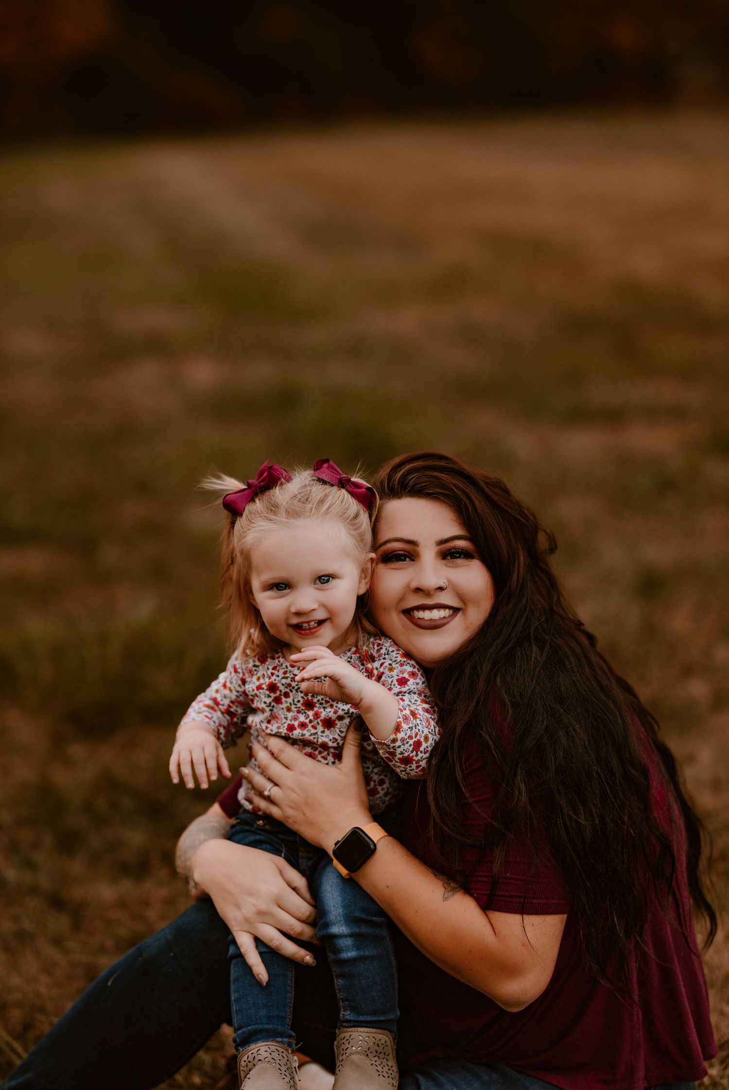 A smiling mother hugging her toddler daughter in an autumn field.