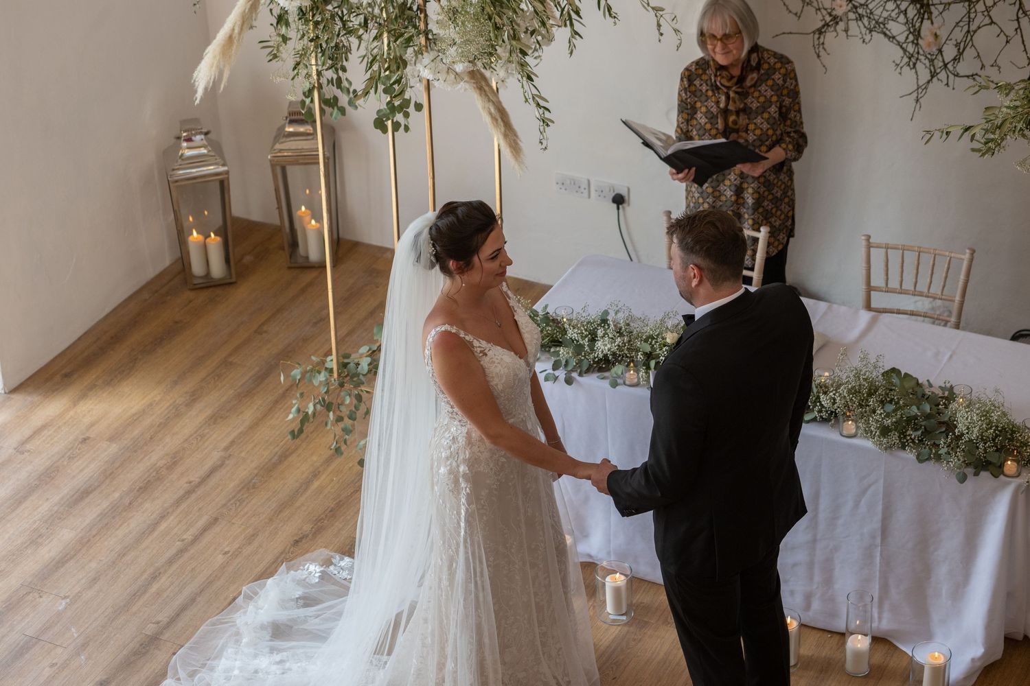 Intimate indoor wedding ceremony with floral arch and lantern decor.