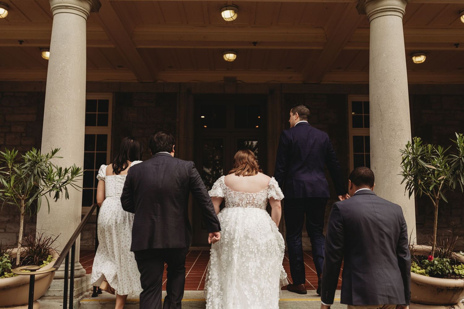 Wedding party entering an elegant columned building with a white dress trailing behind.