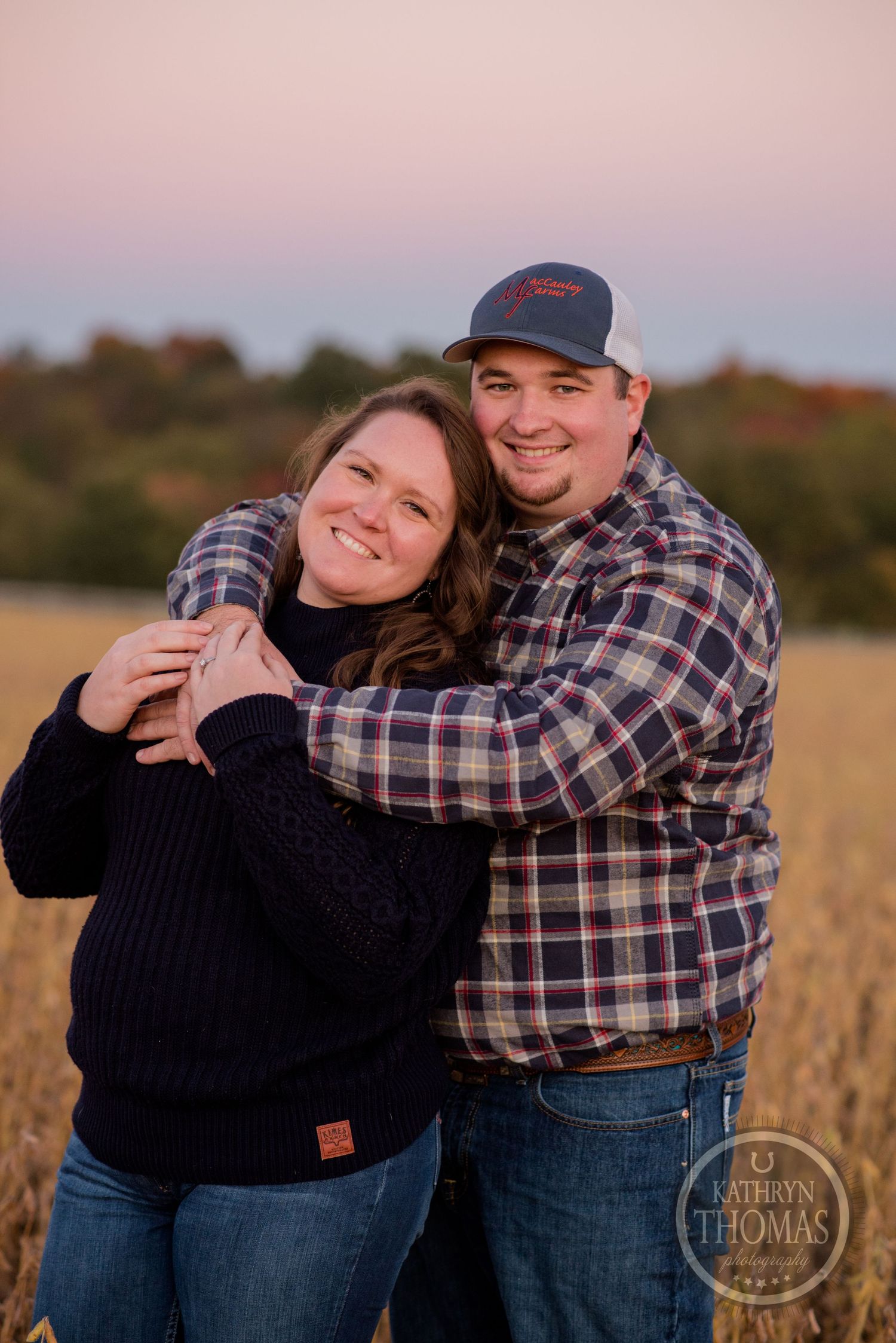 Happy couple in casual outdoor wear embracing in autumn field at dusk.