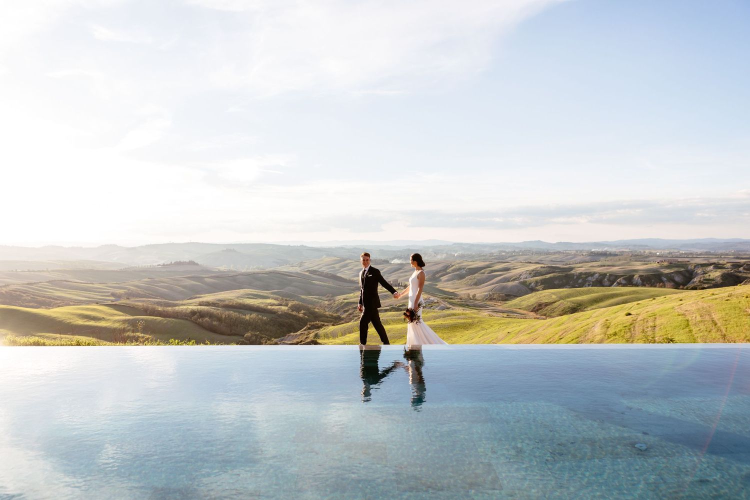 Romantic wedding photography, a couple walk by the pool at the Lazy Olive, the Tuscany hills in the background.