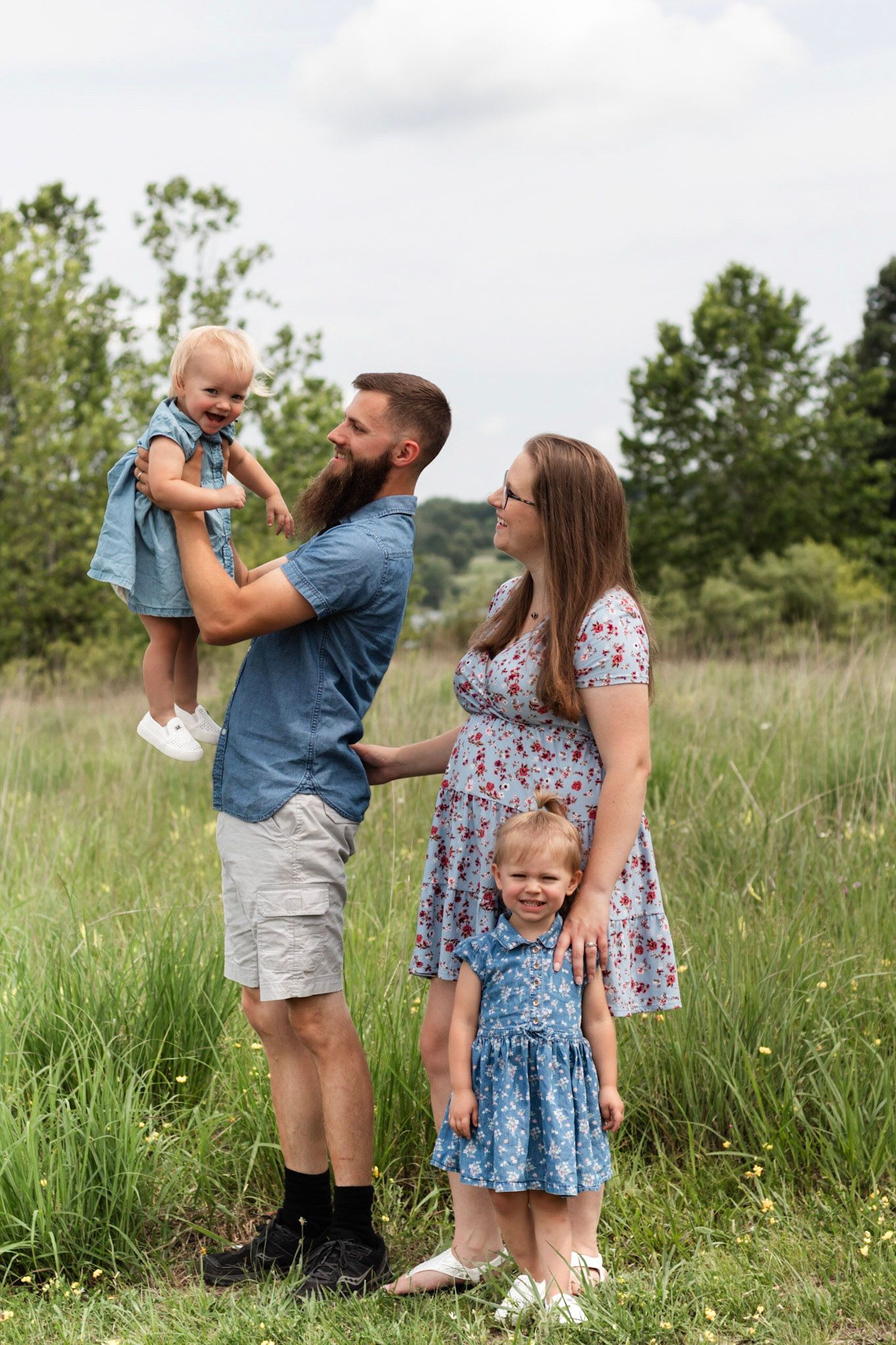 Family of four posing together in sunny meadow for outdoor portrait.