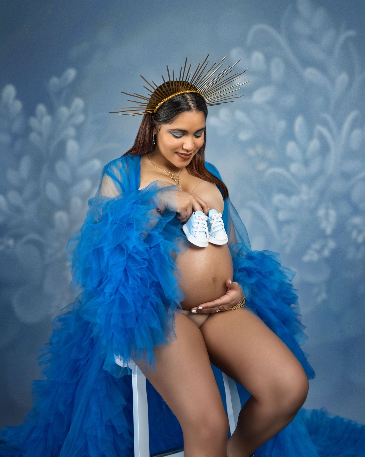 Dramatic maternity portrait with electric blue feathers and gold crown headpiece.