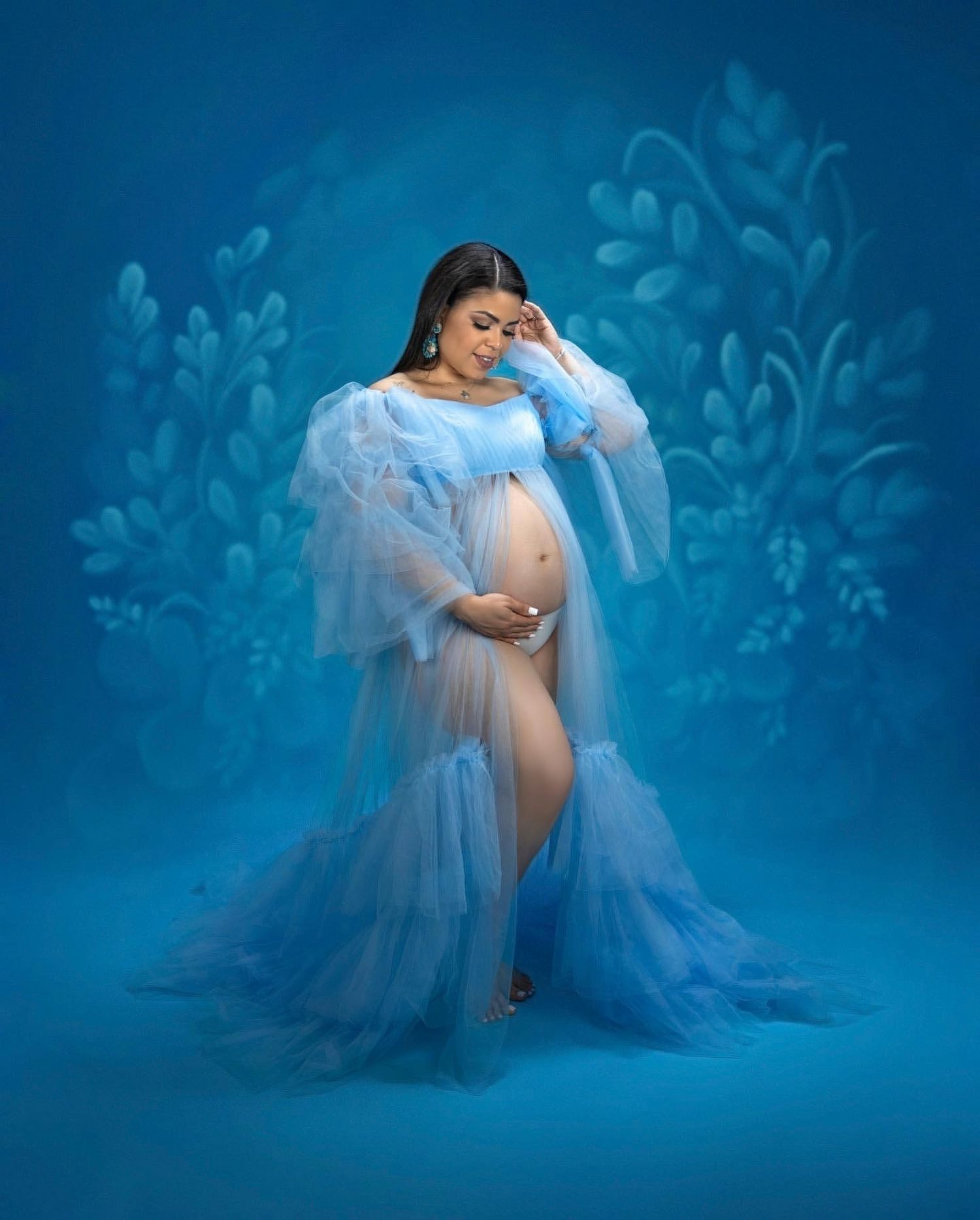 Artistic maternity photo with white tulle dress and decorative ladder with floral arrangements.