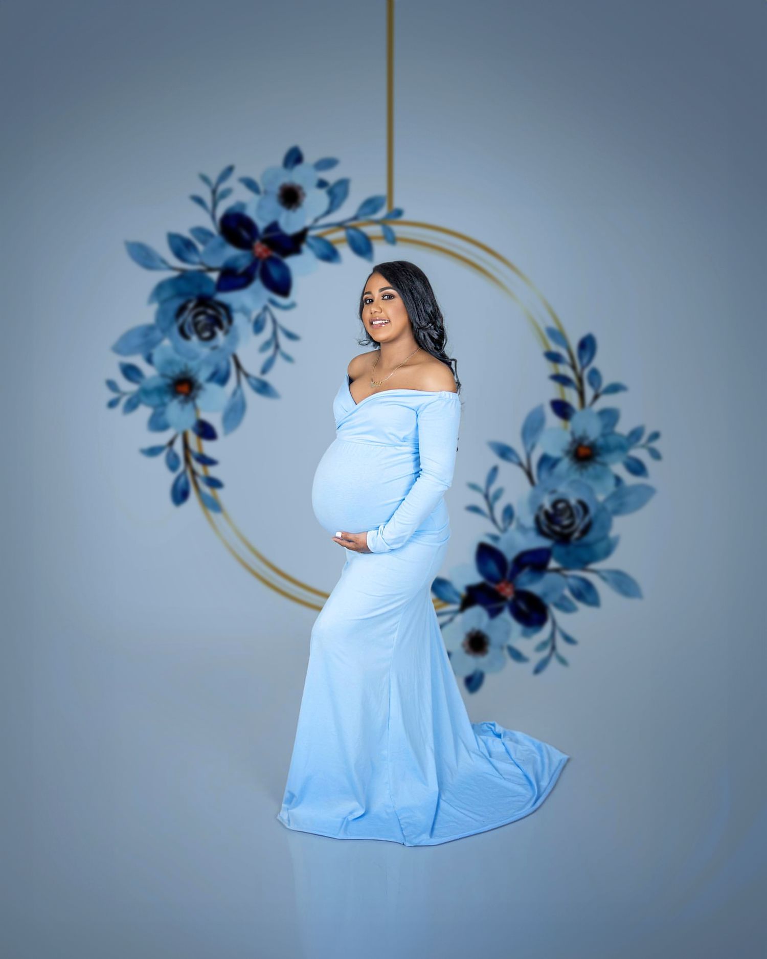 Artistic maternity photo with blue off-shoulder dress against floral circular backdrop.