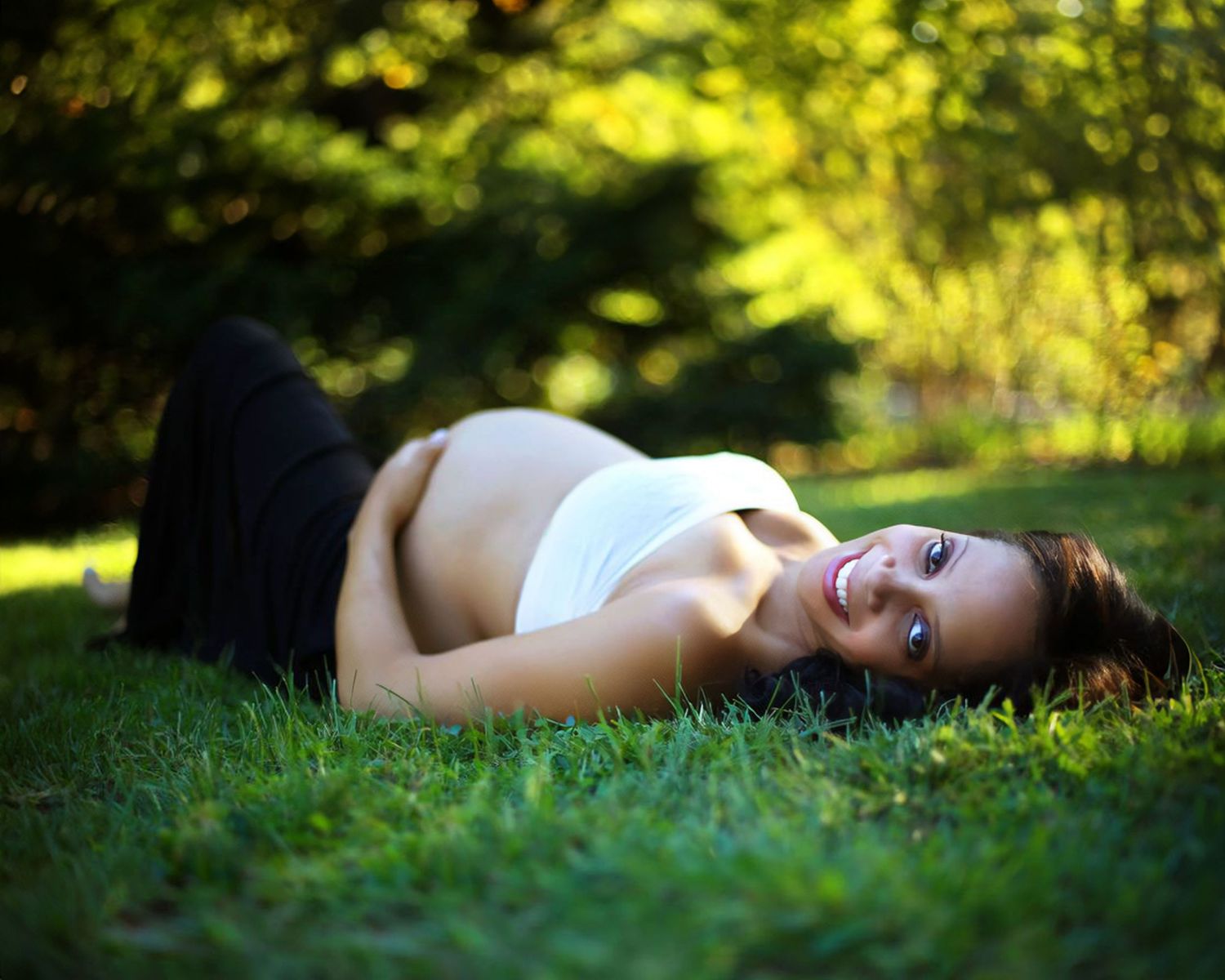 Maternity photo of expectant mother laying in grass with natural lighting.