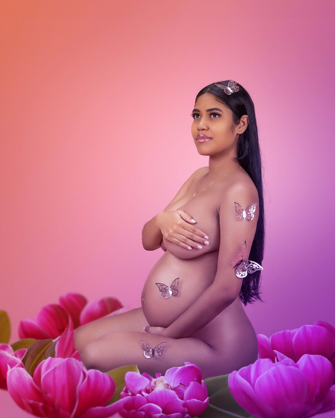 Artistic maternity photo with butterfly details and pink floral backdrop.