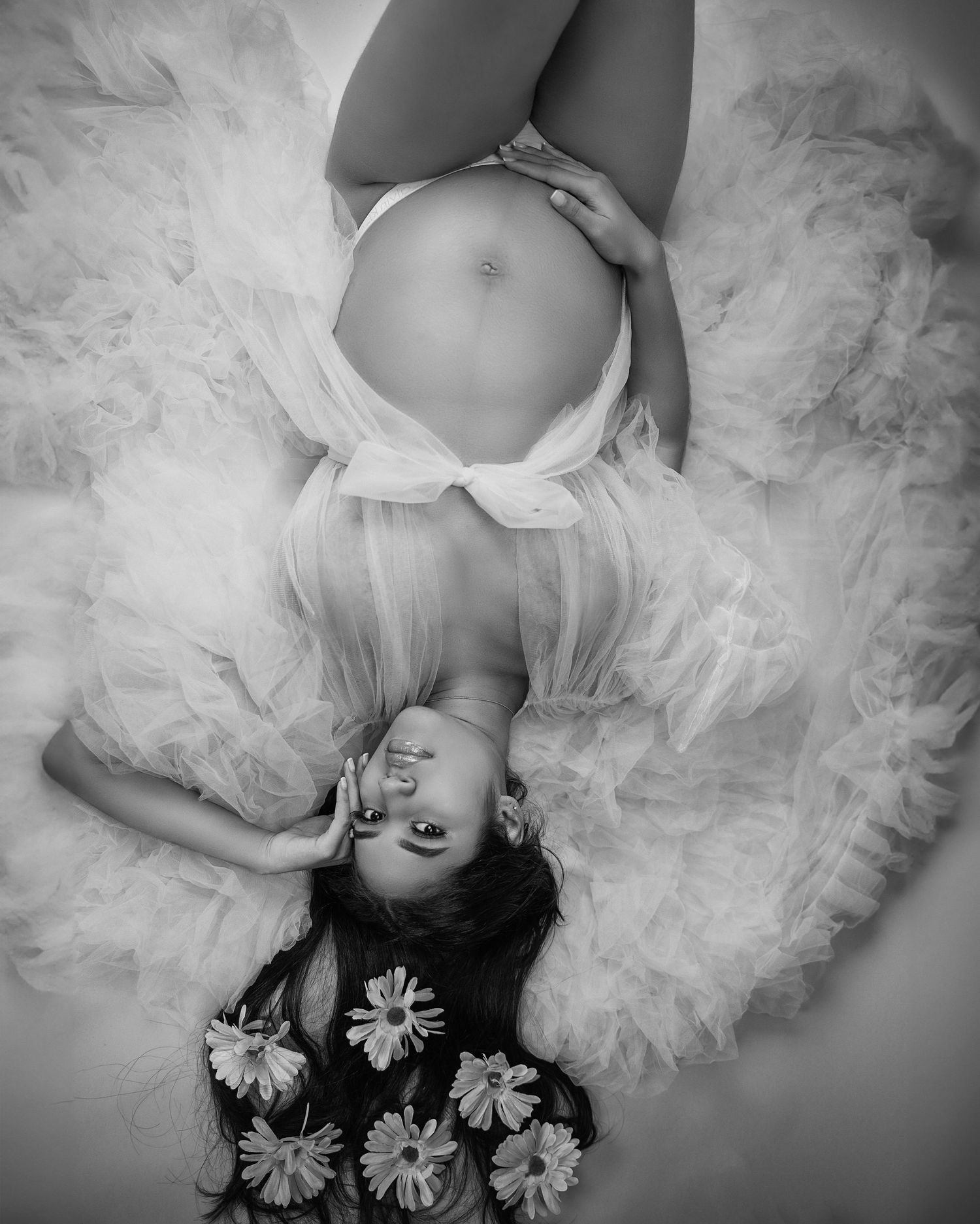 Black and white overhead maternity photo with tulle dress and floral elements.