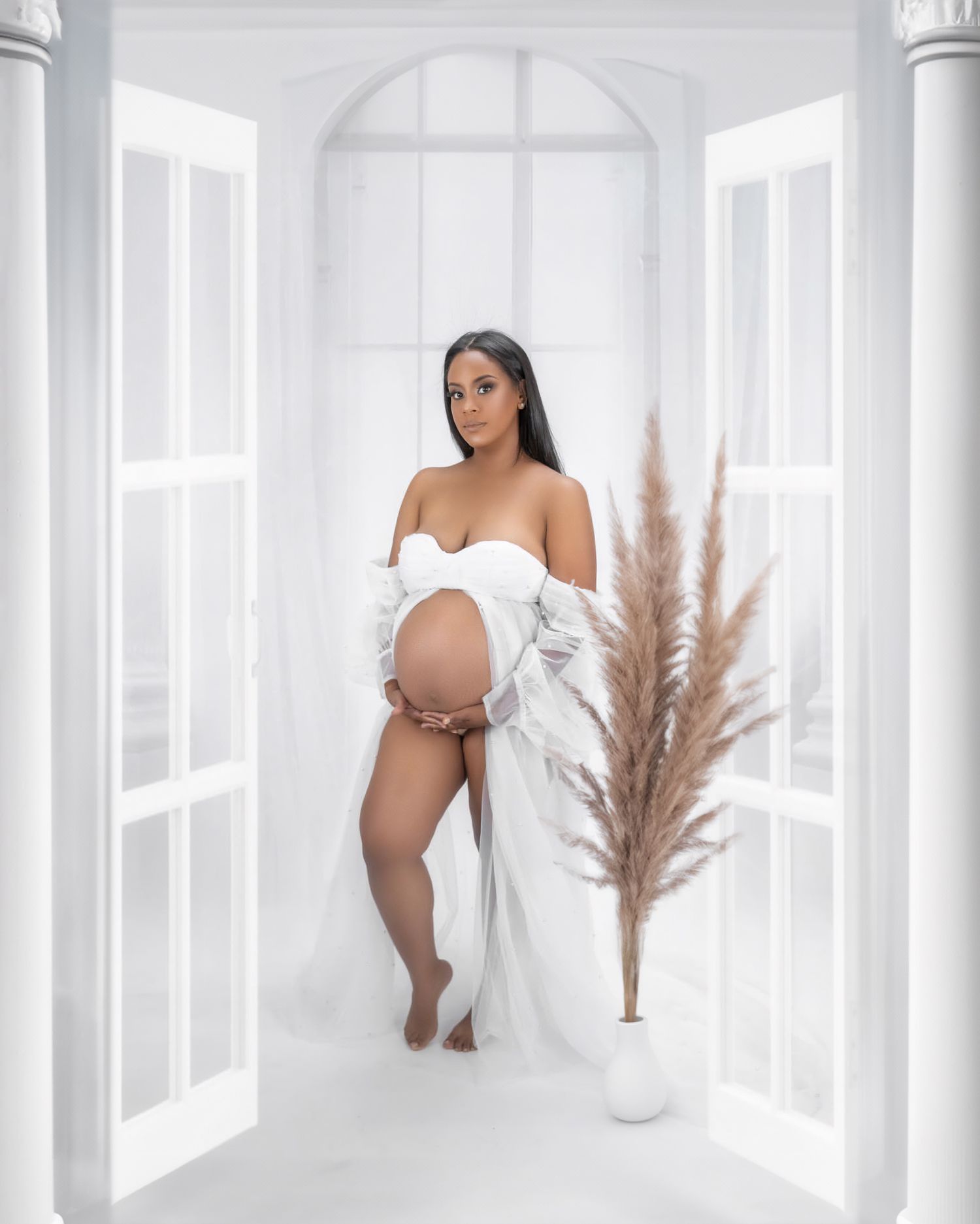 Elegant maternity portrait in white dress against bright architectural setting with pampas grass.