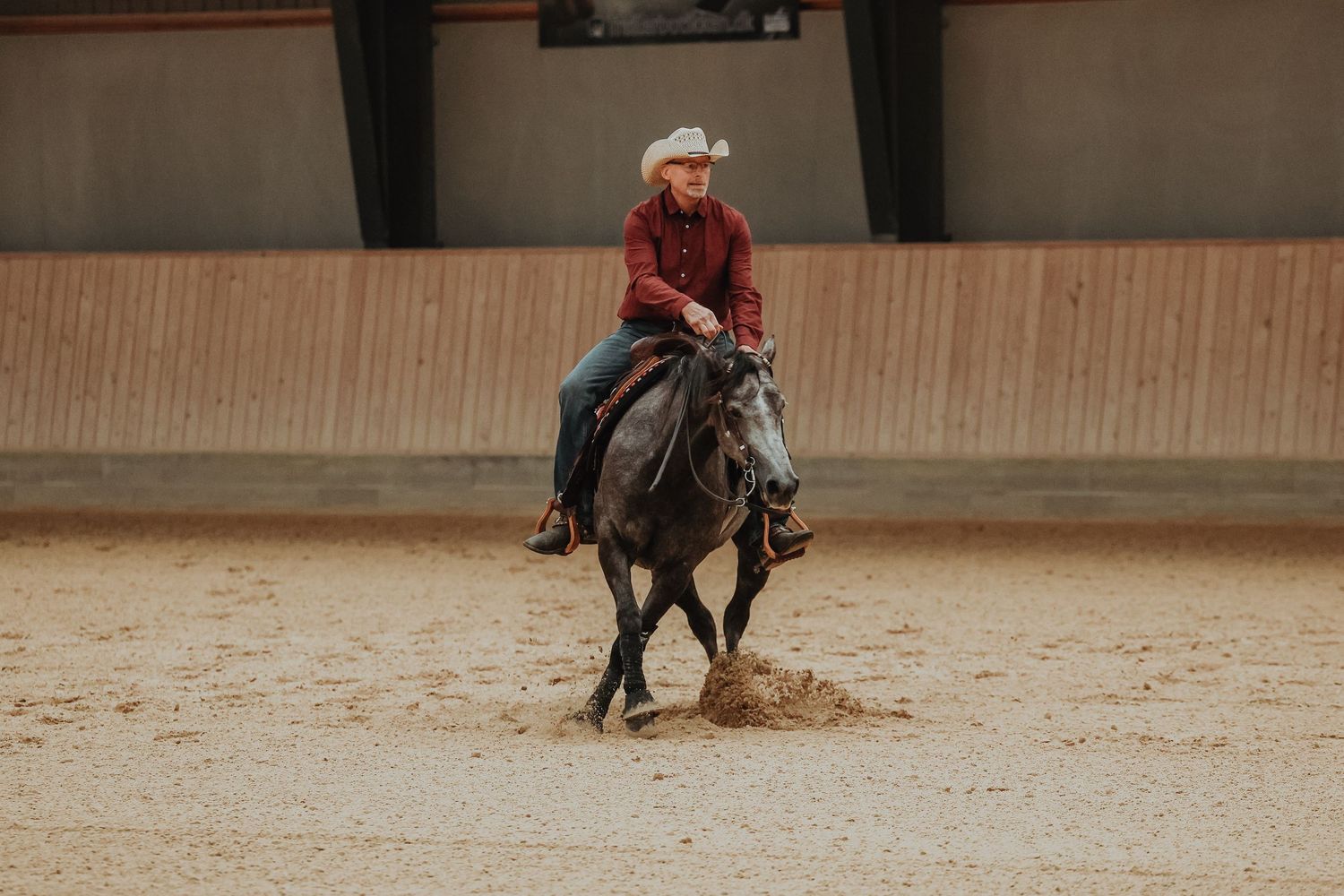 Horse and rider practicing western riding techniques in an indoor arena with wooden walls.
