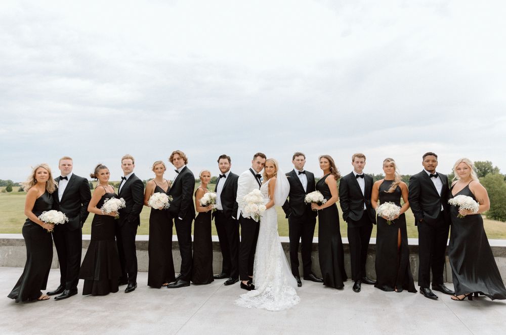 Wedding party in black and white attire poses together in a long line outdoors.