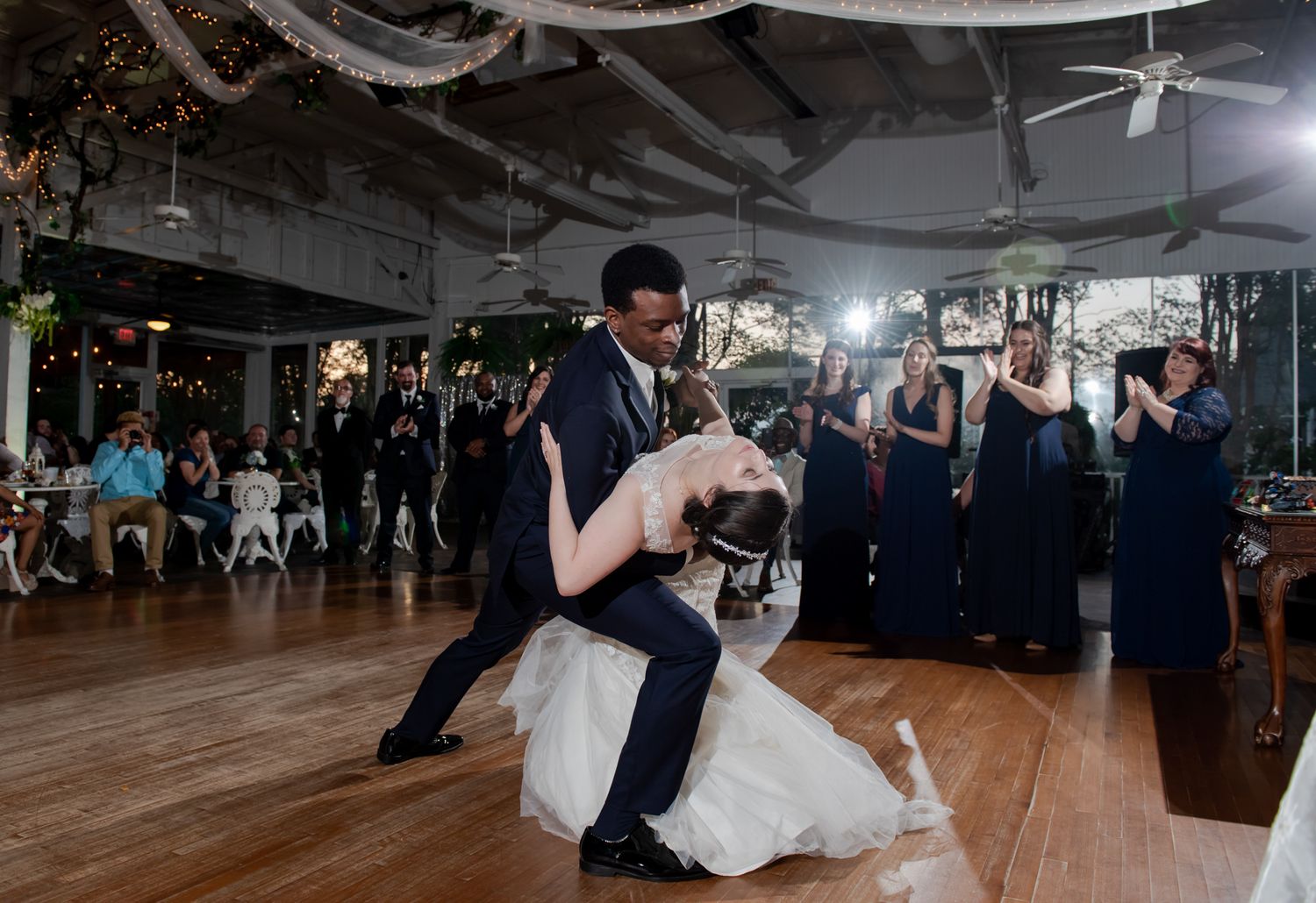 Wedding couple performs dramatic dip during first dance at reception with guests watching.