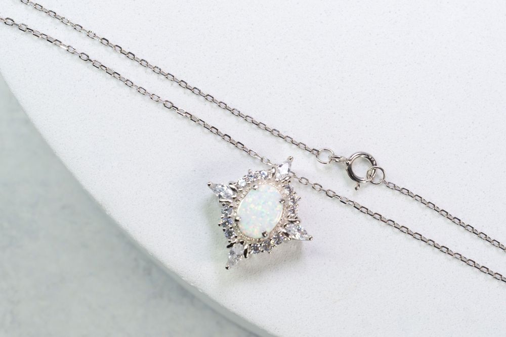 A delicate silver necklace with crystal pendant displayed on a curved white surface.