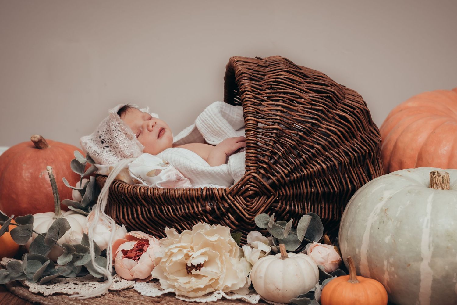 baby sleeps in moses basket surrounded by pumpkins and flowers for in-home themed newborn session