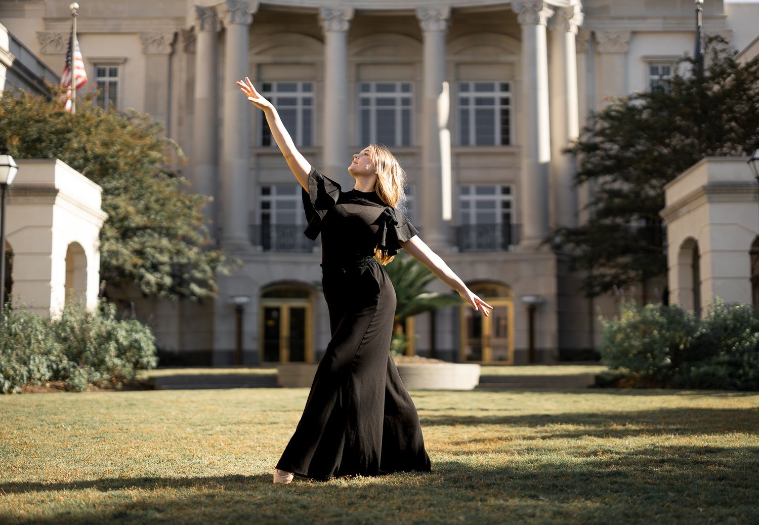 Figure in flowing black dress striking dramatic pose in front of grand columned building.