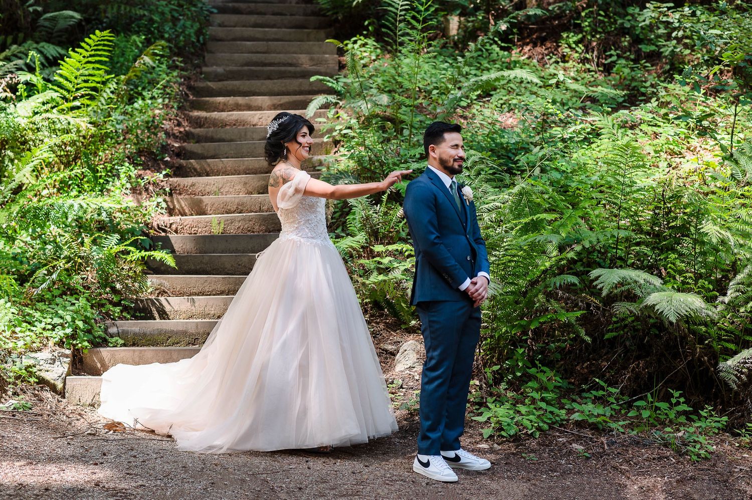 A playful first look moment on woodland stairs surrounded by natural greenery.