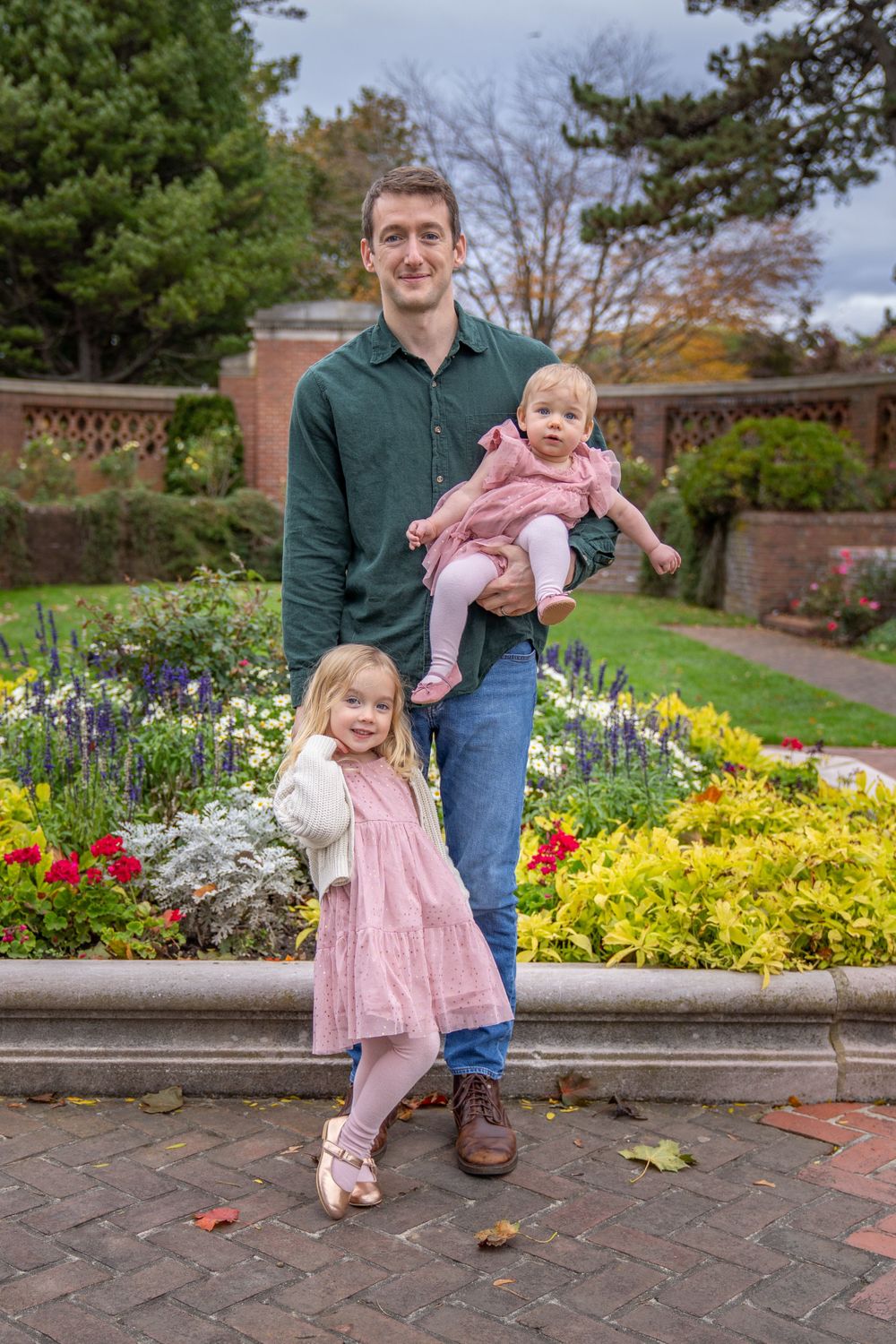 Family portrait in colorful garden with blooming flowers and brick wall backdrop.