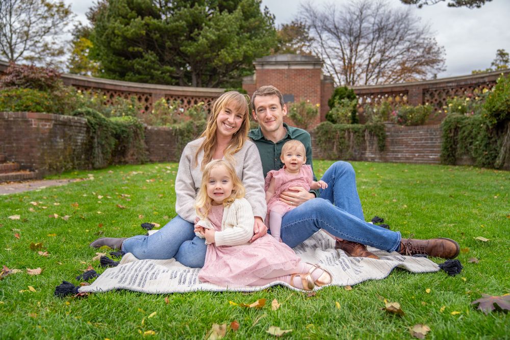 Family sitting together on blanket in garden with brick wall and greenery background.