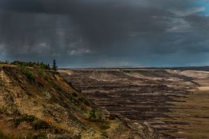 Storm clouds gather over a vast open pit mine with dramatic cliffs and industrial landscape.