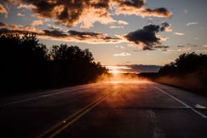 Dramatic sunset illuminates empty rural highway with golden light and dark clouds.