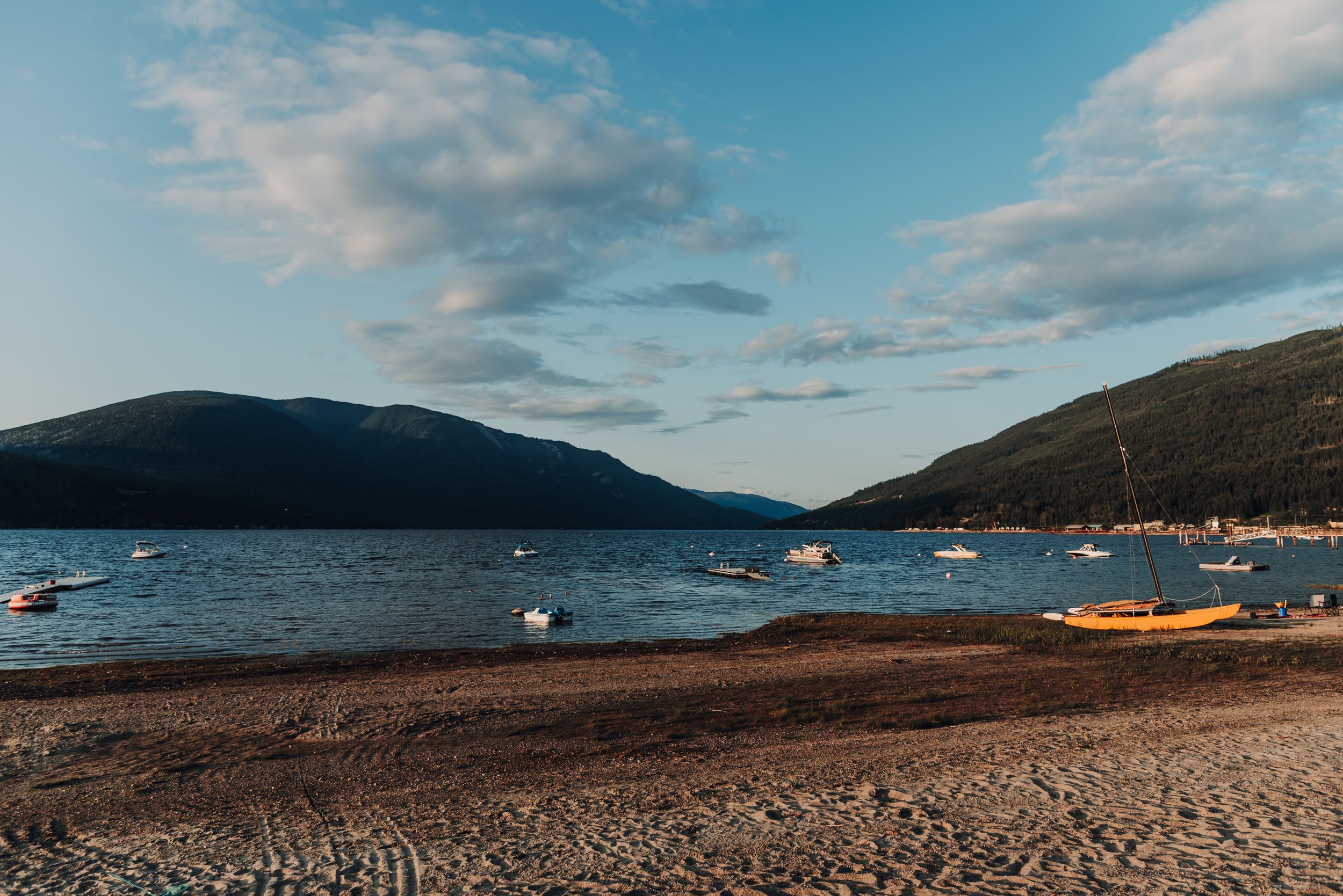 Mountain lake shore with boats and buoys under blue summer skies.