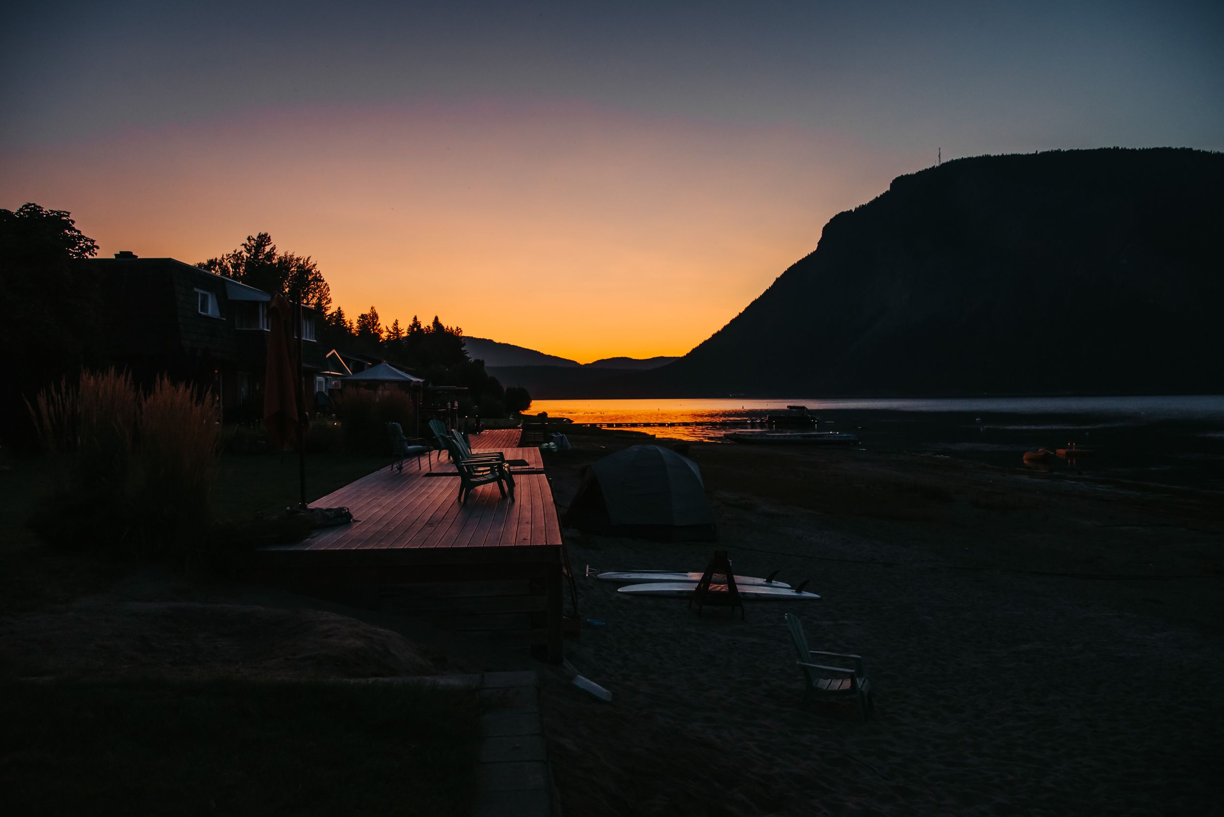 Silhouetted boats and docks at sunset with mountain backdrop.