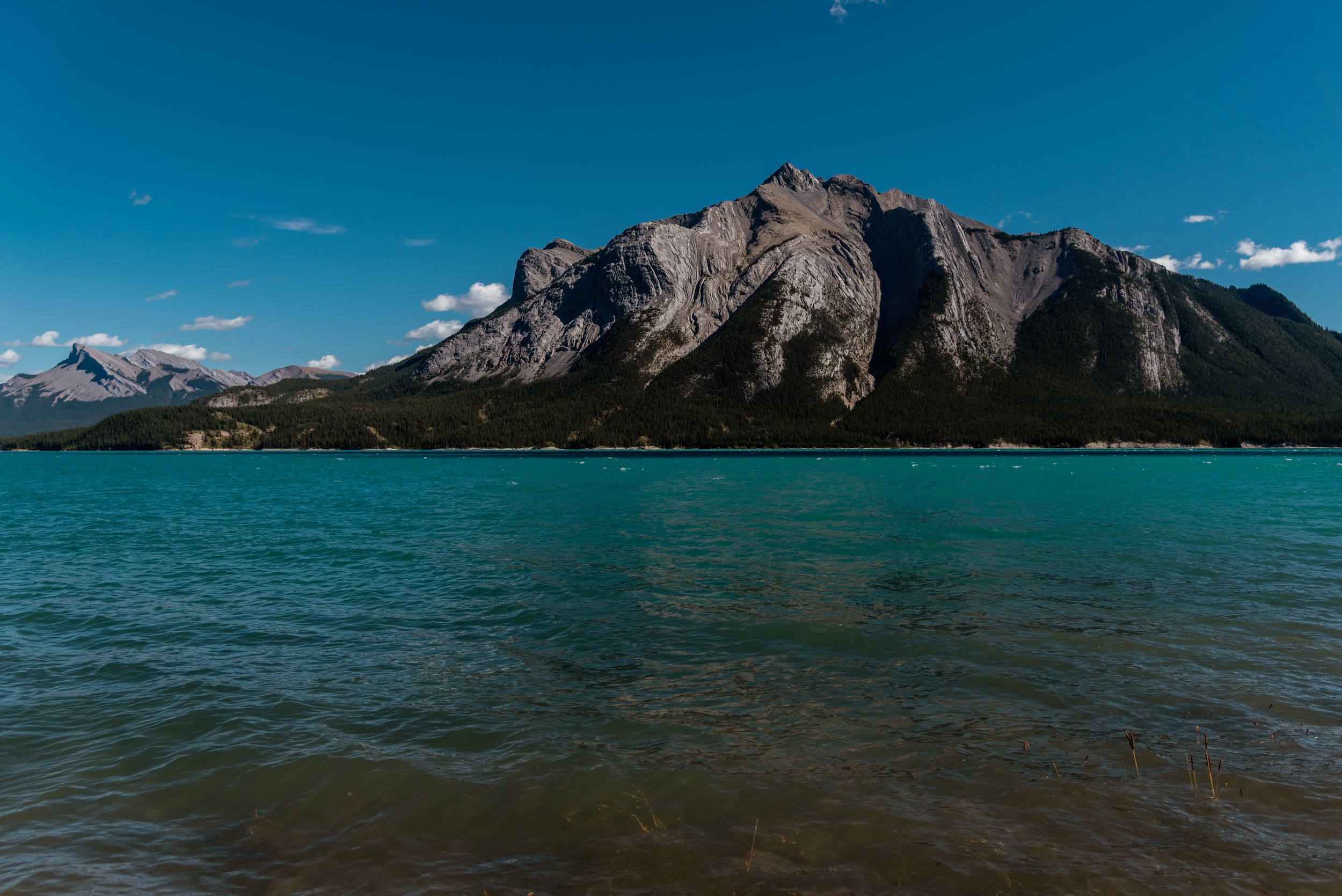 Turquoise mountain lake surrounded by dramatic rocky peaks under blue sky.