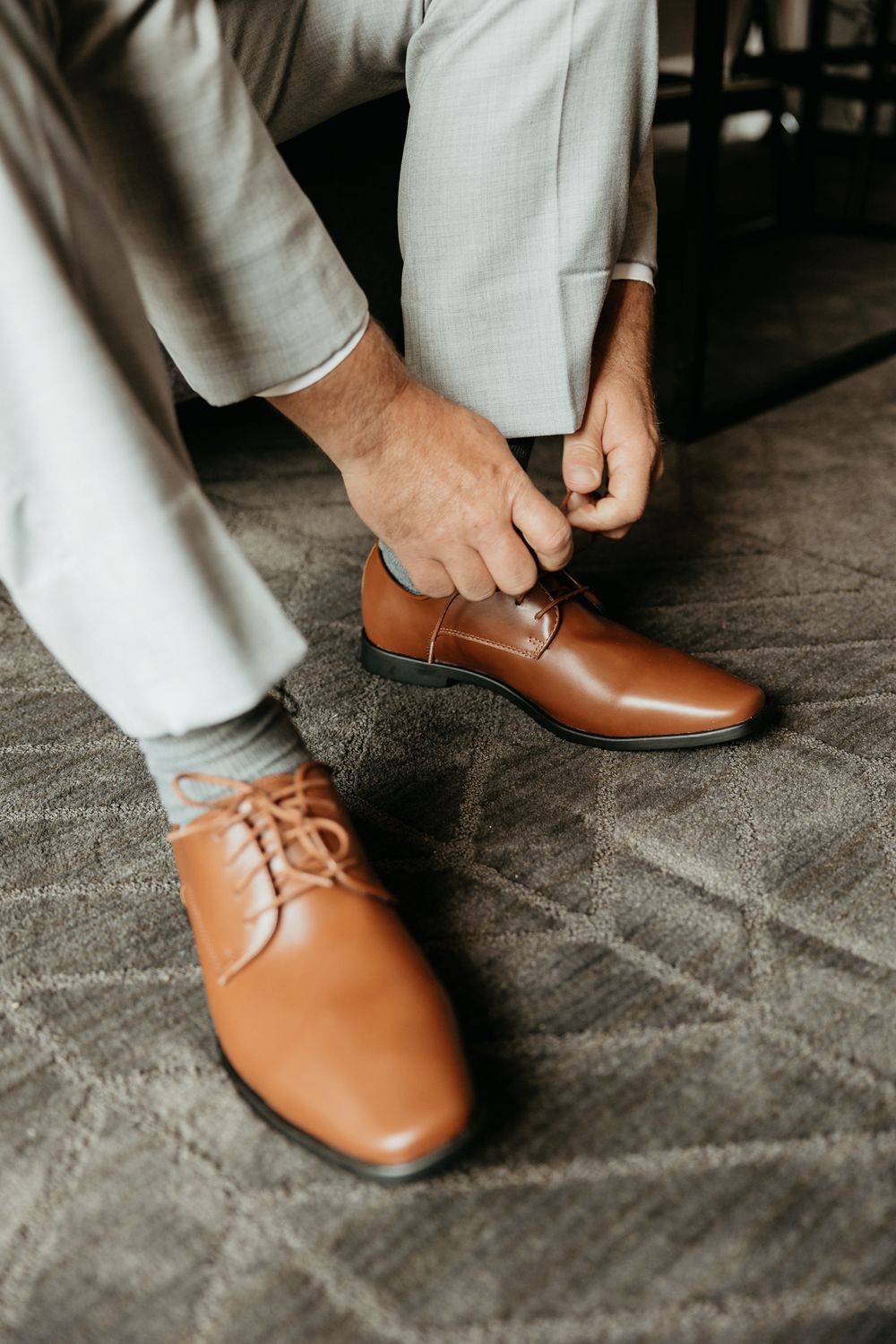 Close-up of tan leather dress shoes being fastened on light carpet.