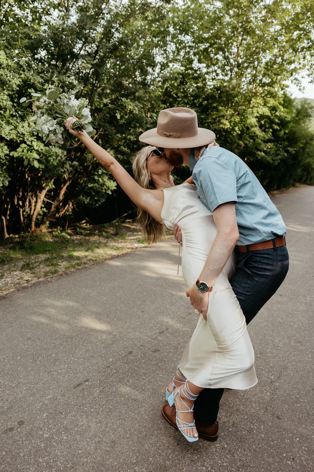 Romantic couple dancing on pathway wearing western hat and elegant white dress.