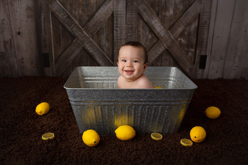Happy baby in galvanized tub with lemons against rustic wooden background.