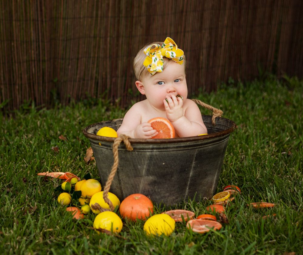 Charming bath time setup with citrus fruits scattered around a vintage metal tub on grass.