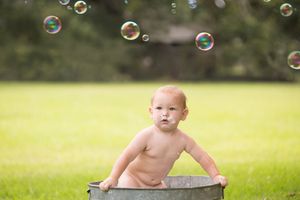 Playful outdoor bath scene with floating bubbles and metal tub in a sunny garden.