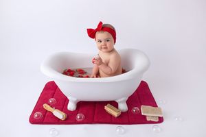 Classic bath photography setup with white tub, red bow, and rustic wooden props.