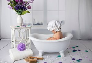 Bath setup with white tub, purple flowers in vase, and bath accessories on light background.