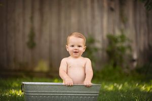 Baby in galvanized metal tub outdoors against wooden fence in garden setting.