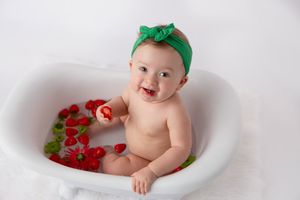 Baby in white tub with green headband and scattered red rose petals.