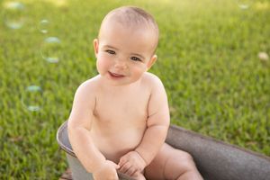 Joyful baby sitting outdoors on a sunny day with green grass in the background.