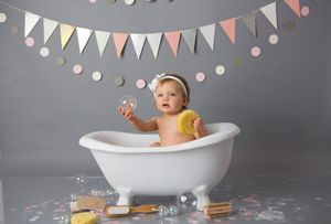 Vintage white bathtub with pastel bunting and yellow decor against grey backdrop.