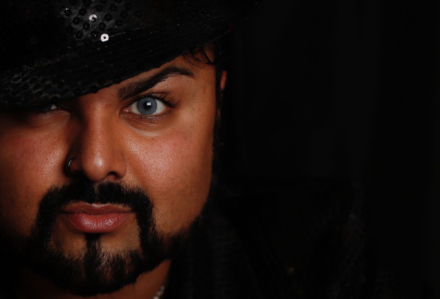 Close-up portrait of someone wearing a black hat against a dark background.